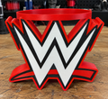 Red, black, and white WWE candle holder with a circular top opening on a wooden workbench.