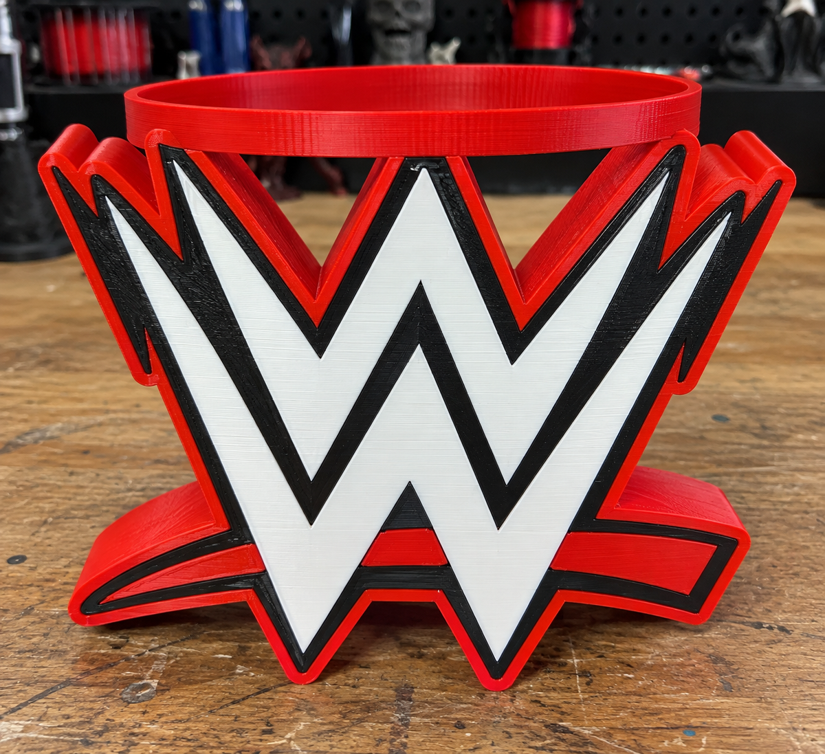 Red, black, and white WWE candle holder with a circular top opening on a wooden workbench.