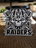 Black-and-white Las Vegas Raiders candle holder with a helmeted skull, crossed blades, and Raiders lettering on a tabletop.