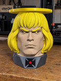 He-Man candle holder with yellow hair, a gray emblem base, and a yellow circular top tray on a workbench.