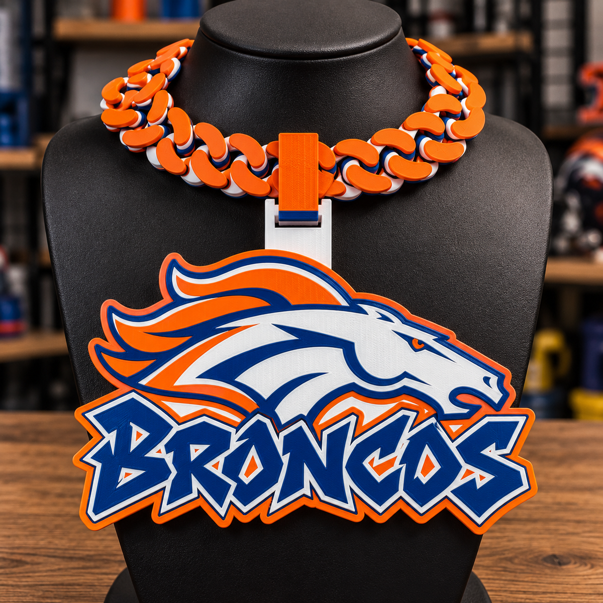 Orange, navy, and white Broncos hype chain with horse-head emblem and Broncos lettering on a black display bust.