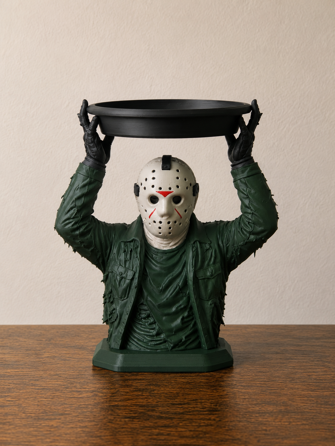 Jason Voorhees figure in a green jacket holding a black circular candle tray overhead on a rectangular base.