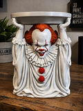 Pennywise candle holder with orange hair, white costume, red accents, and raised hands supporting a circular tray.