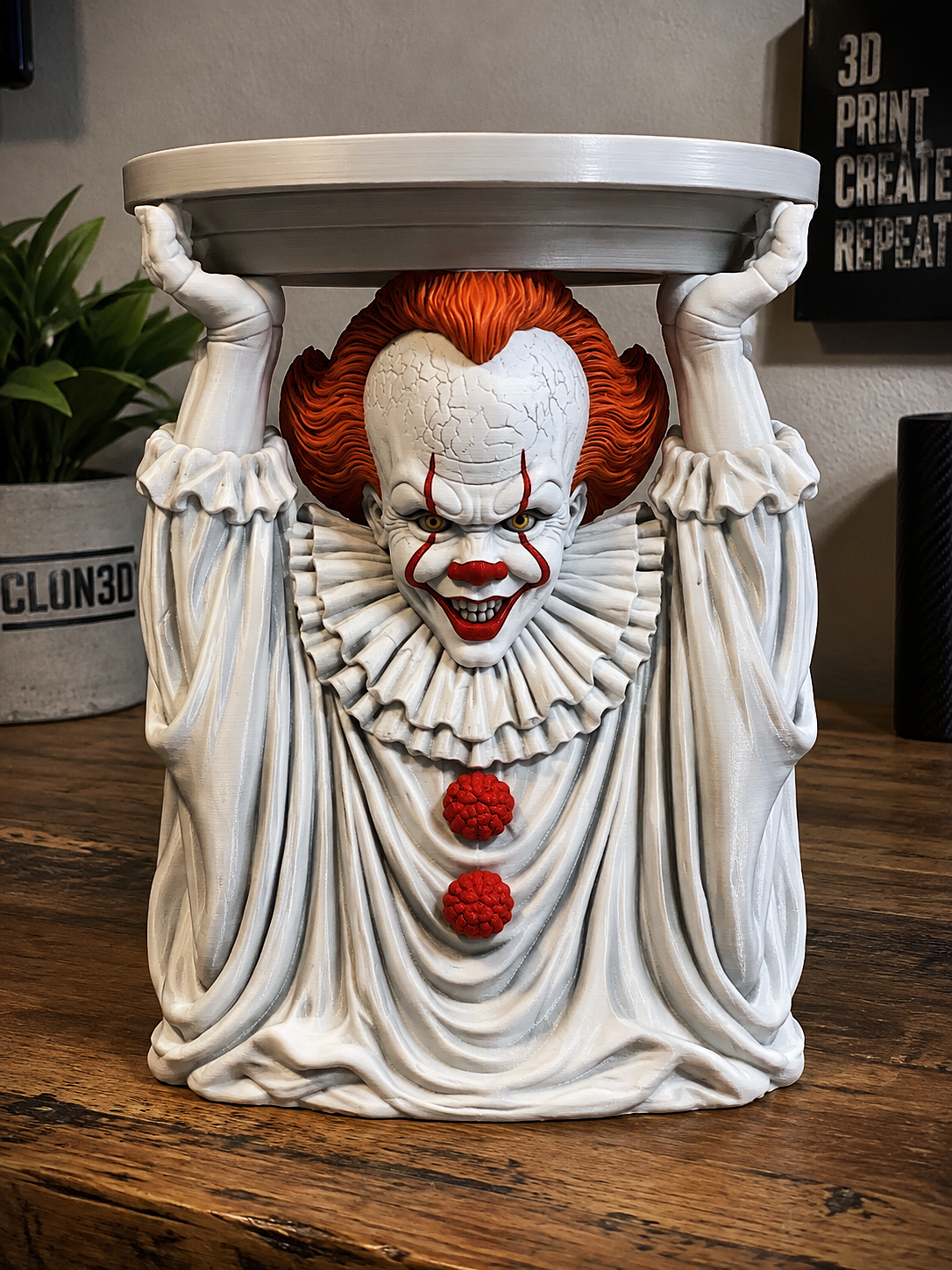 Pennywise candle holder with orange hair, white costume, red accents, and raised hands supporting a circular tray.