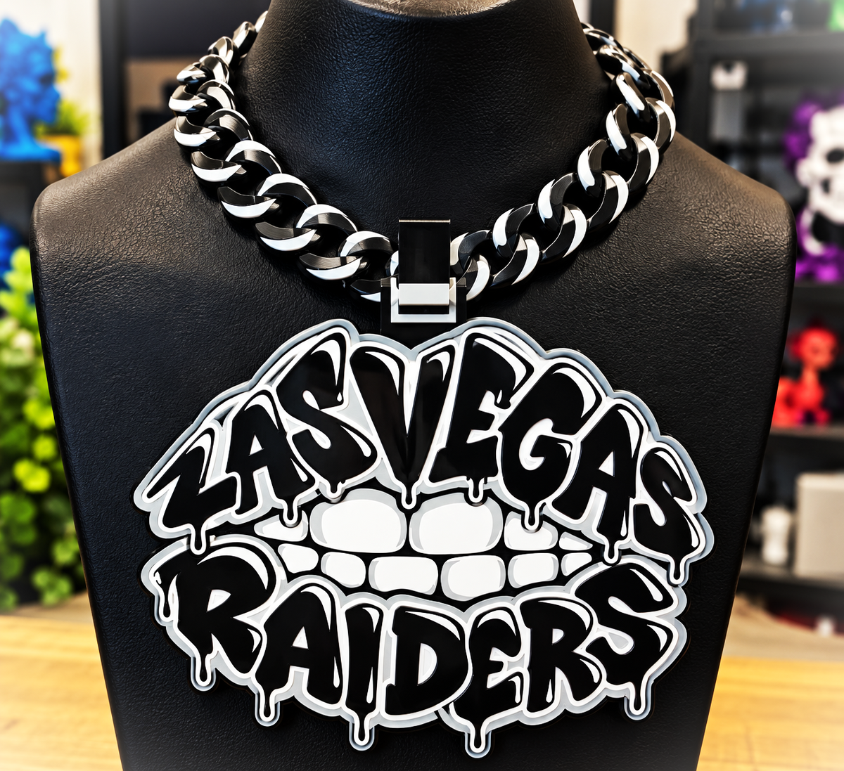 Black-and-white Las Vegas Raiders Lip hype chain with teeth and dripping graffiti-style lettering on a black display bust.