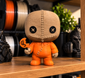 Sam micro statue with a stitched tan sack-style head, black button eyes, orange outfit, and bitten pumpkin lollipop.