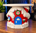 Whoville House candle holder with red walls, a blue door, white snow details, and a white circular top tray on a workbench.